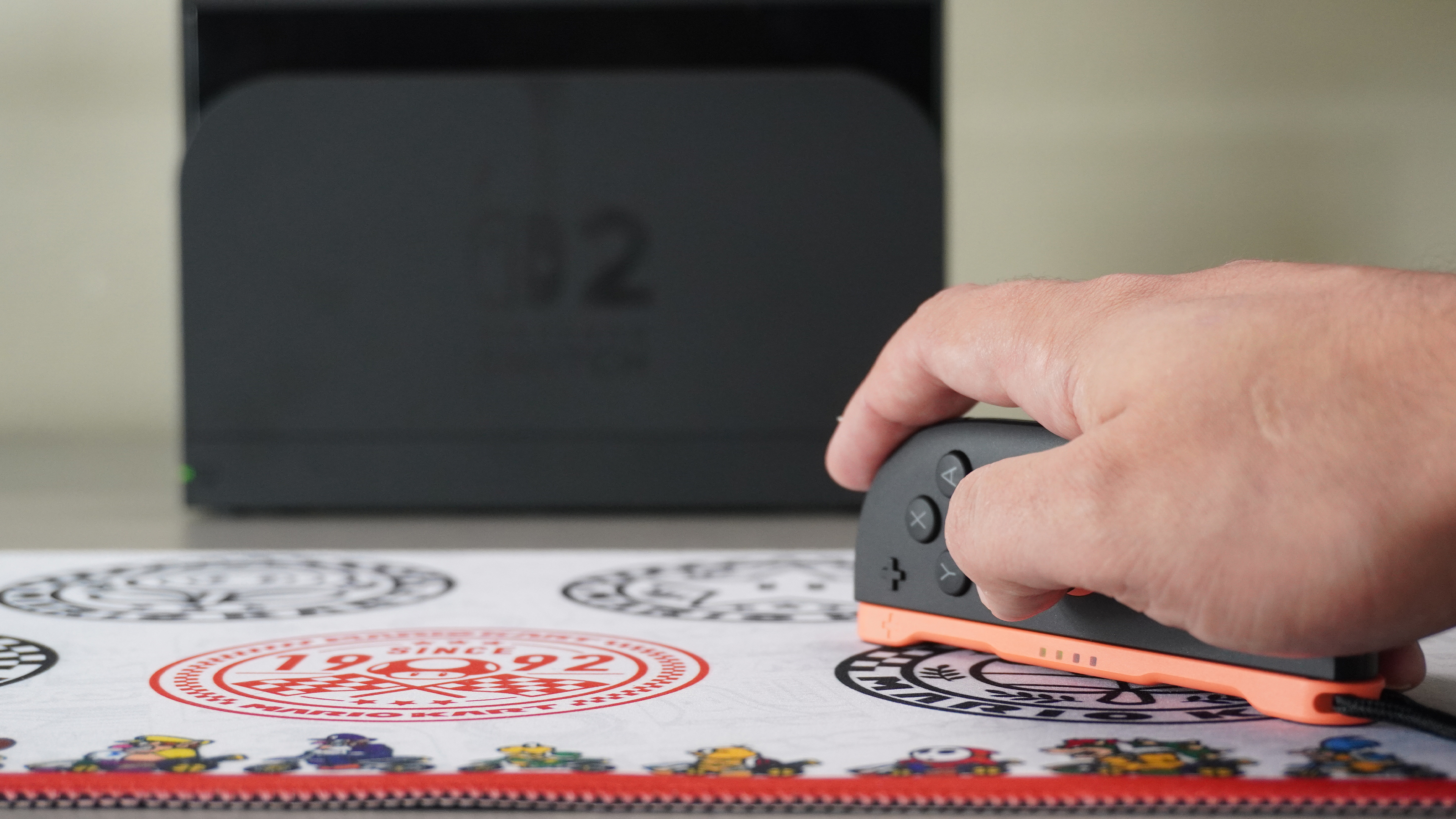 Using a Joy-Con 2 in Mouse Mode on a desk with a docked Switch 2 console in the background