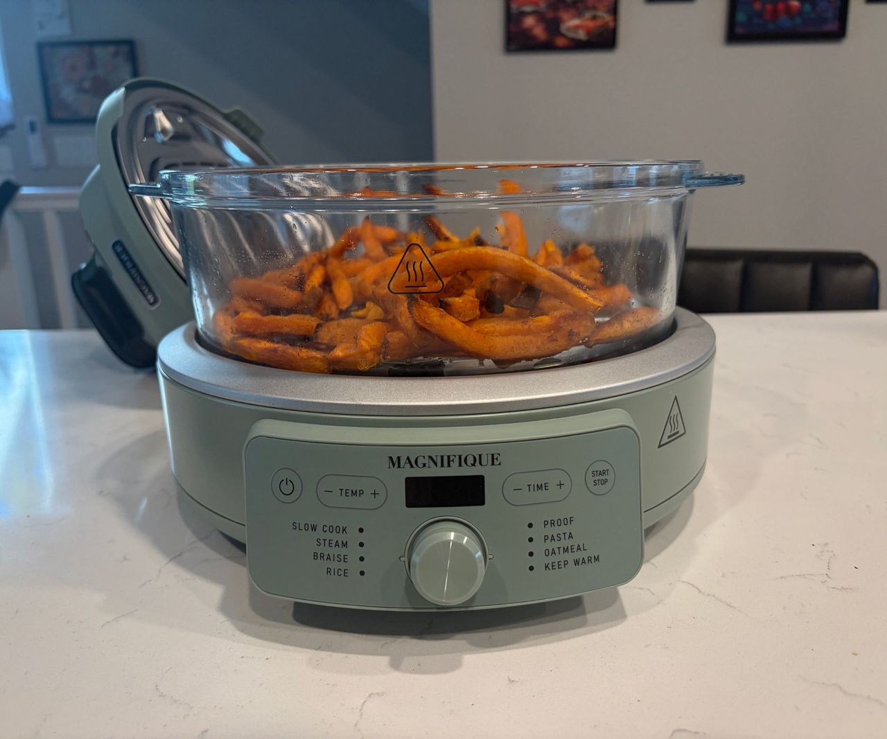 A glass air fryer with a green base on a white countertop filled with sweet potato fries.