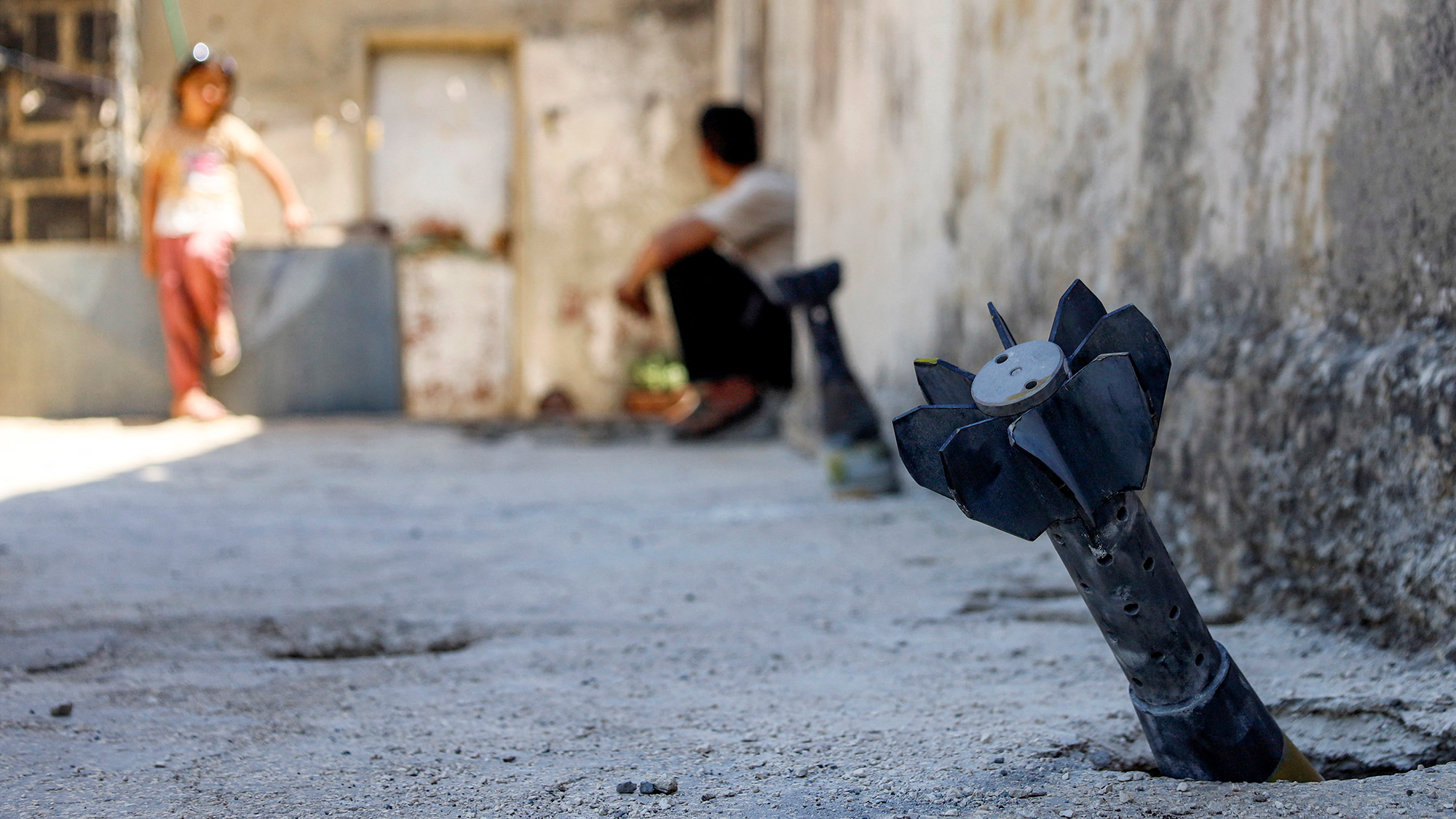 A man speaks with a child while sitting near an unexploded artillery shell from an overnight Israeli bombardment in Abidin, Syria
