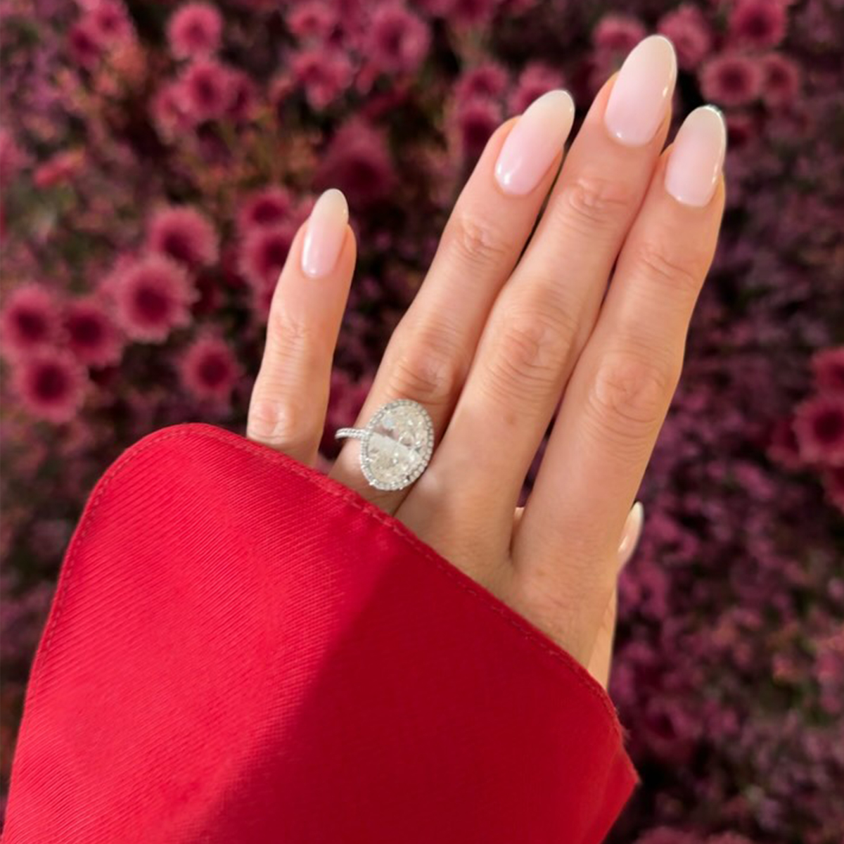 A close-up Elsa Hosk's hands with a red shirt cuff, an oval engagement ring and long almond nails with a sheer milky pink nail colour
