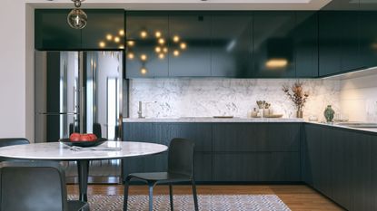 A dark gree kitchen with glossy cabinets and a white marble backsplash