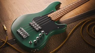 The Cort GB Short-scale Bass finished in green, photographed against a light wooden floor and rug.