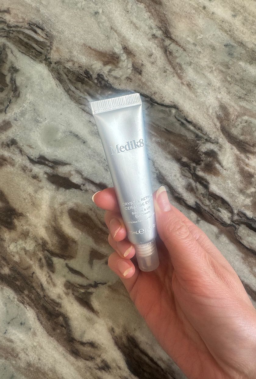 A picture of Eleanor holding the Medik8 Crystal Retinal Ceramide eye cream on a marble background