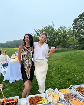 Leah McCarthy stands with Gigi Hadid at a friends' cookout for a birthday, where Gigi Hadid demonstrates how to style a silk slip skirt