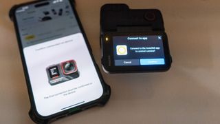 Insta360 Ace Pro 2 next to iPhone on table with screens showing that they are linking wirelessly – 'Connect to app' approval button is on Ace Pro 2 touchscreen