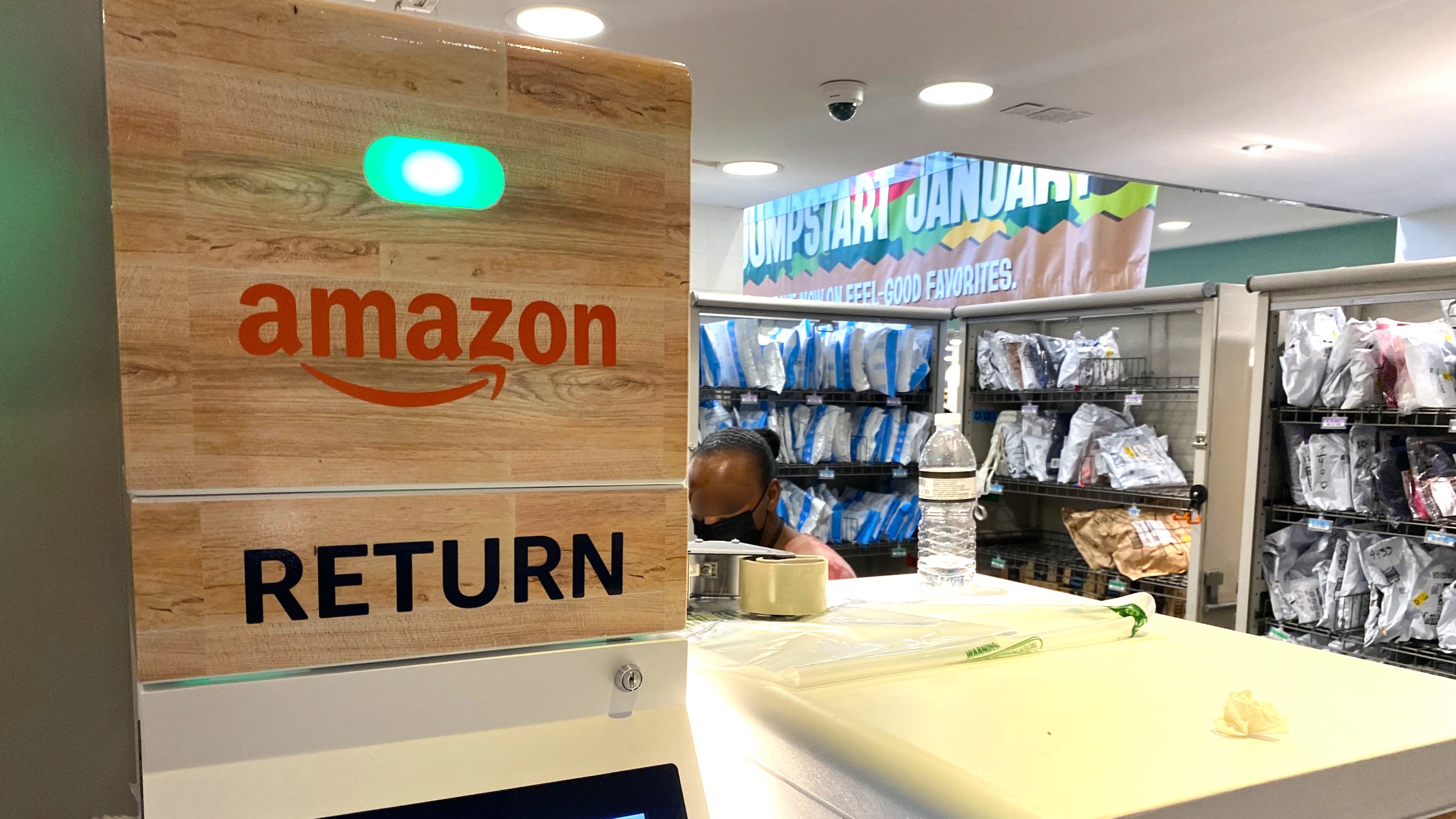 An Amazon return kiosk positioned next to rows of shelves with Amazon packages.