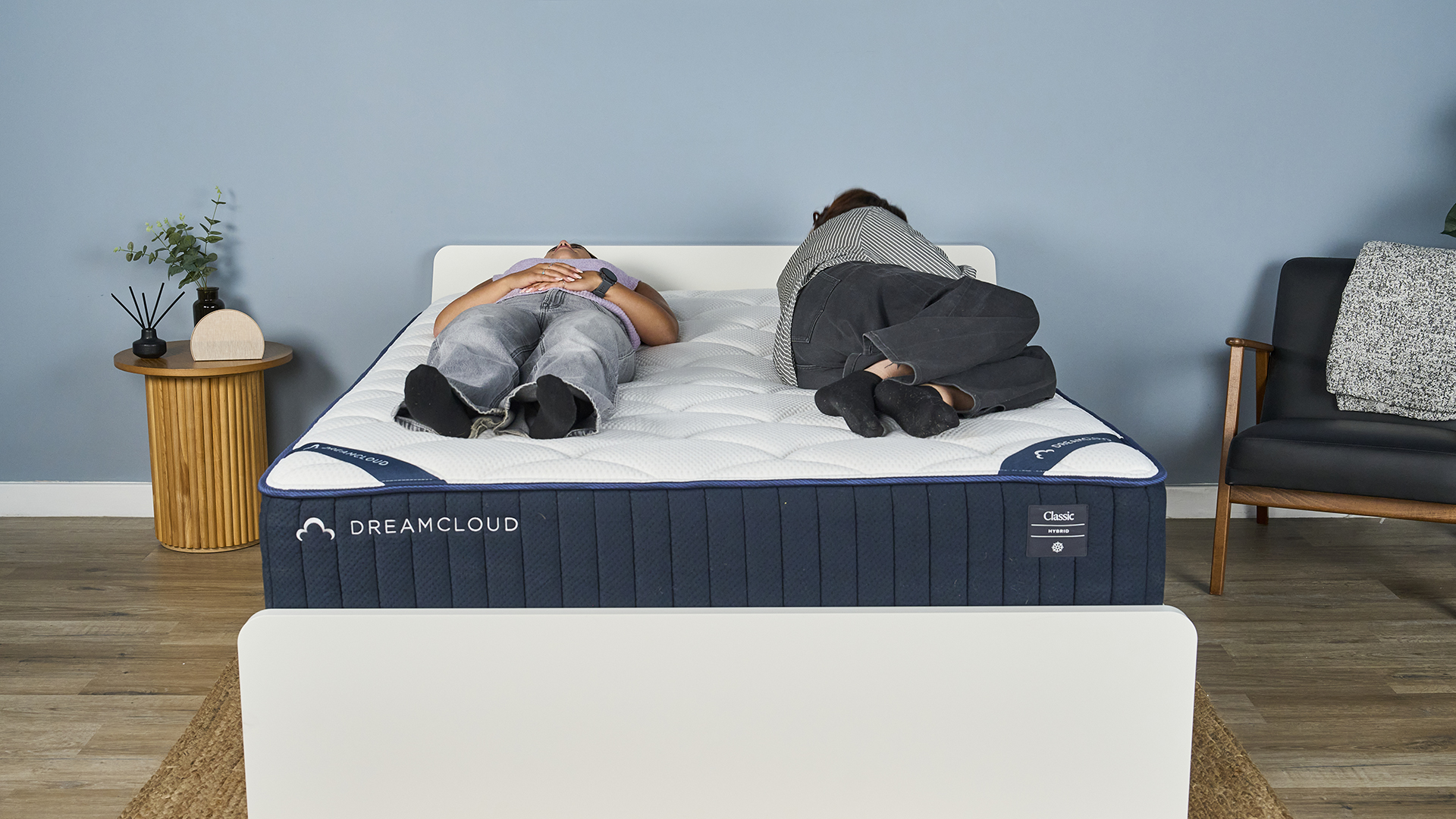 One Tom's Guide tester lies on her back on the DreamCloud Classic inside a blue-painted bedroom while another gets into bed, lies on her side and then lies on her other side