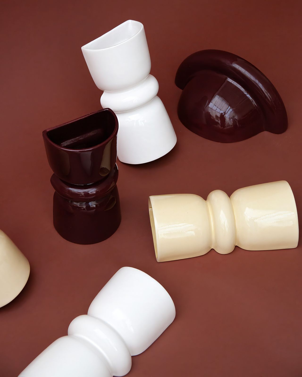 A group of sculptural sconces in white, butter yellow, and burgundy red on a brick red background.