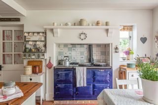 blue aga in kitchen with red quarry tiles and patchwork tablecloth and painted furniture