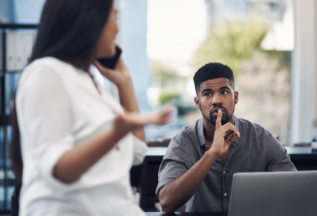 A businessman gesturing for his colleague to be quiet in an office.