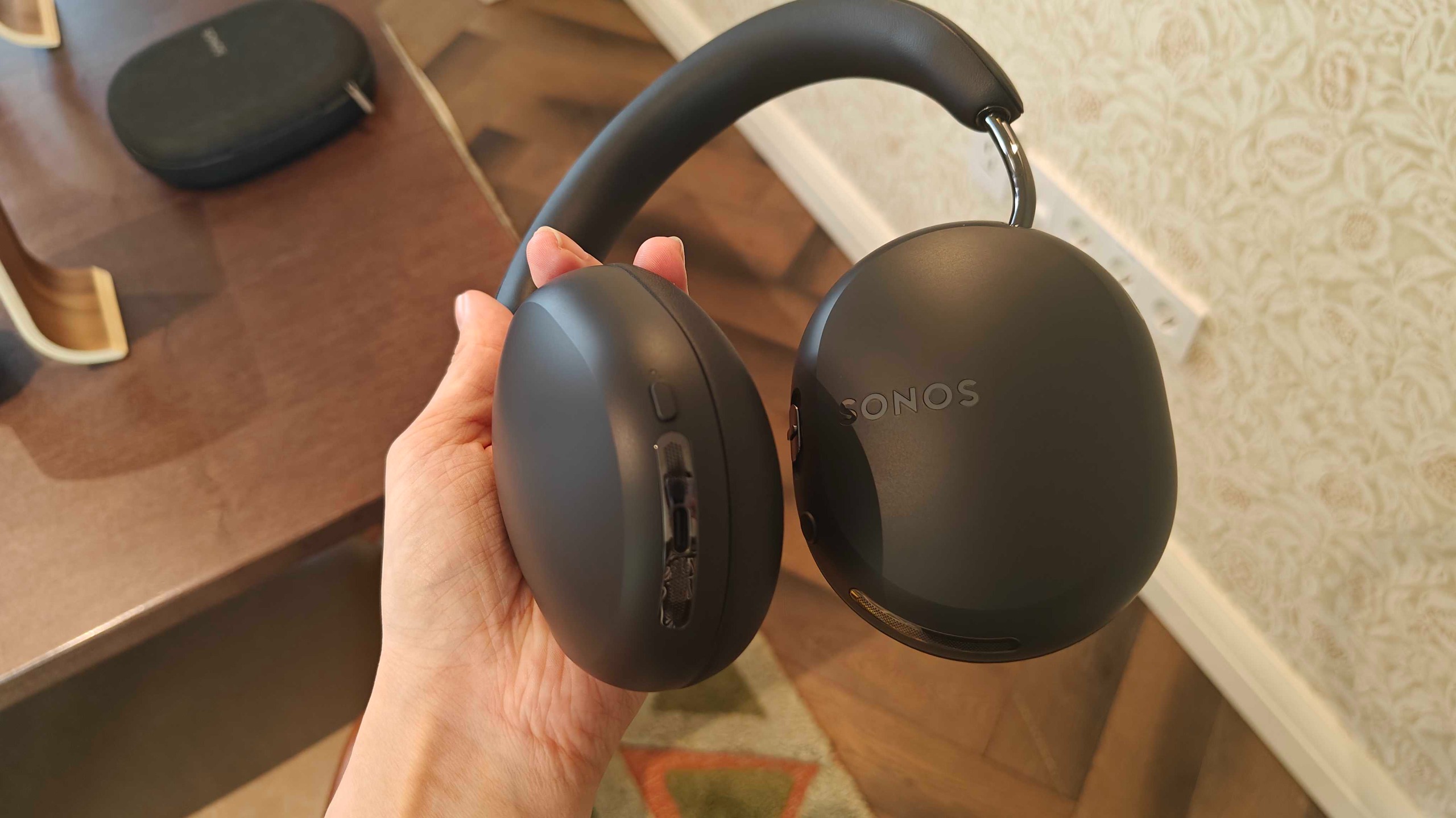 Sonos Ace Ultra being held up over a brown table