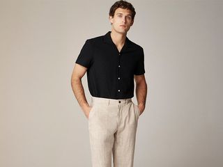 model wears black short sleeve button up top, beige linen trousers, and black loafers