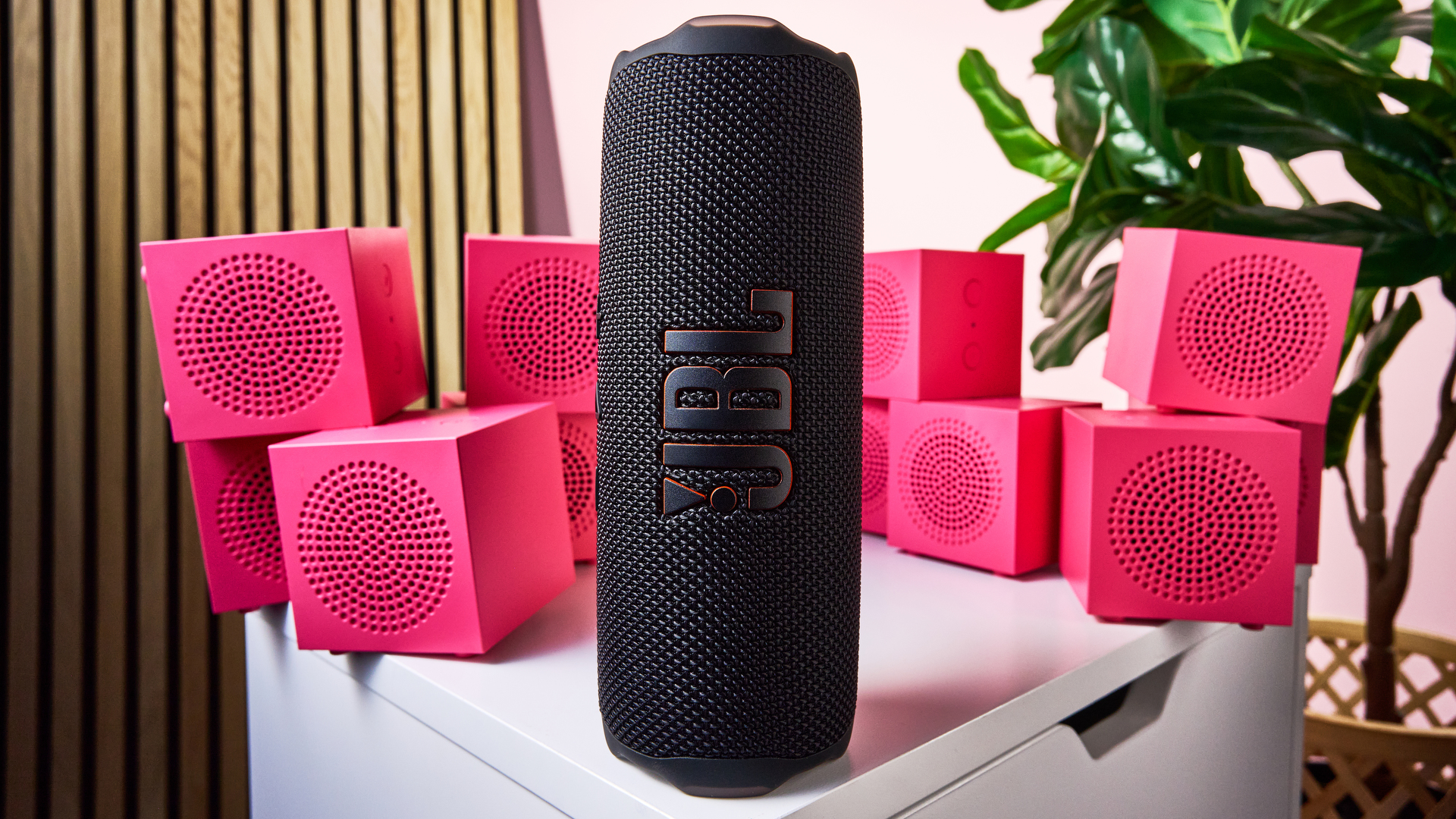 A closeup, wide-angle shot of the JBL Flip 7 in front of stacks of pink IKEA Kallsup speakers.