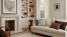 Neuetral living room with cream painted walls, curtains, rug and fitted shelving, tiled fireplace, artworks on walls