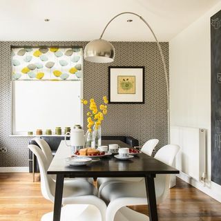 dining area with wooden floorboards, brown and white wallpaper on one wall, a white wall next to it with a section painted with blackboard paint and a black dining table with white chairs