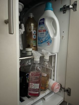 The inside of a cleaning cabinet with laundry detergent, method cleaning sprays, and bin bags