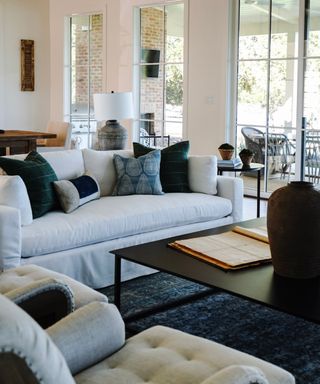 A lake house living room with a white sofa, blue area rug and floor to ceiling windows with a view