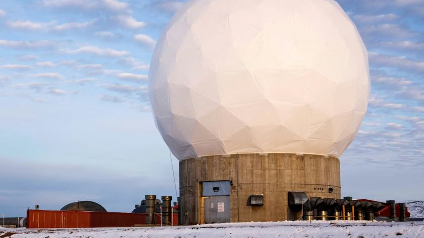 A white geodesic dome sits on top of a circular concrete base surrounded by snow under a cloudy blue sky