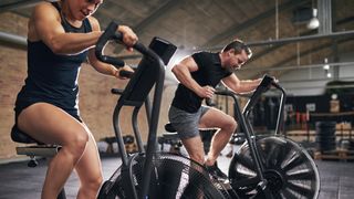 Woman and man using air bikes in gym