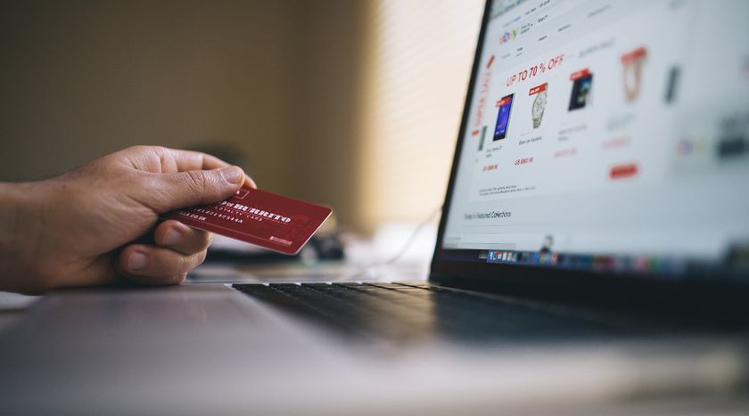 Someone holding a credit card in front of a laptop displaying an ecommerce website.