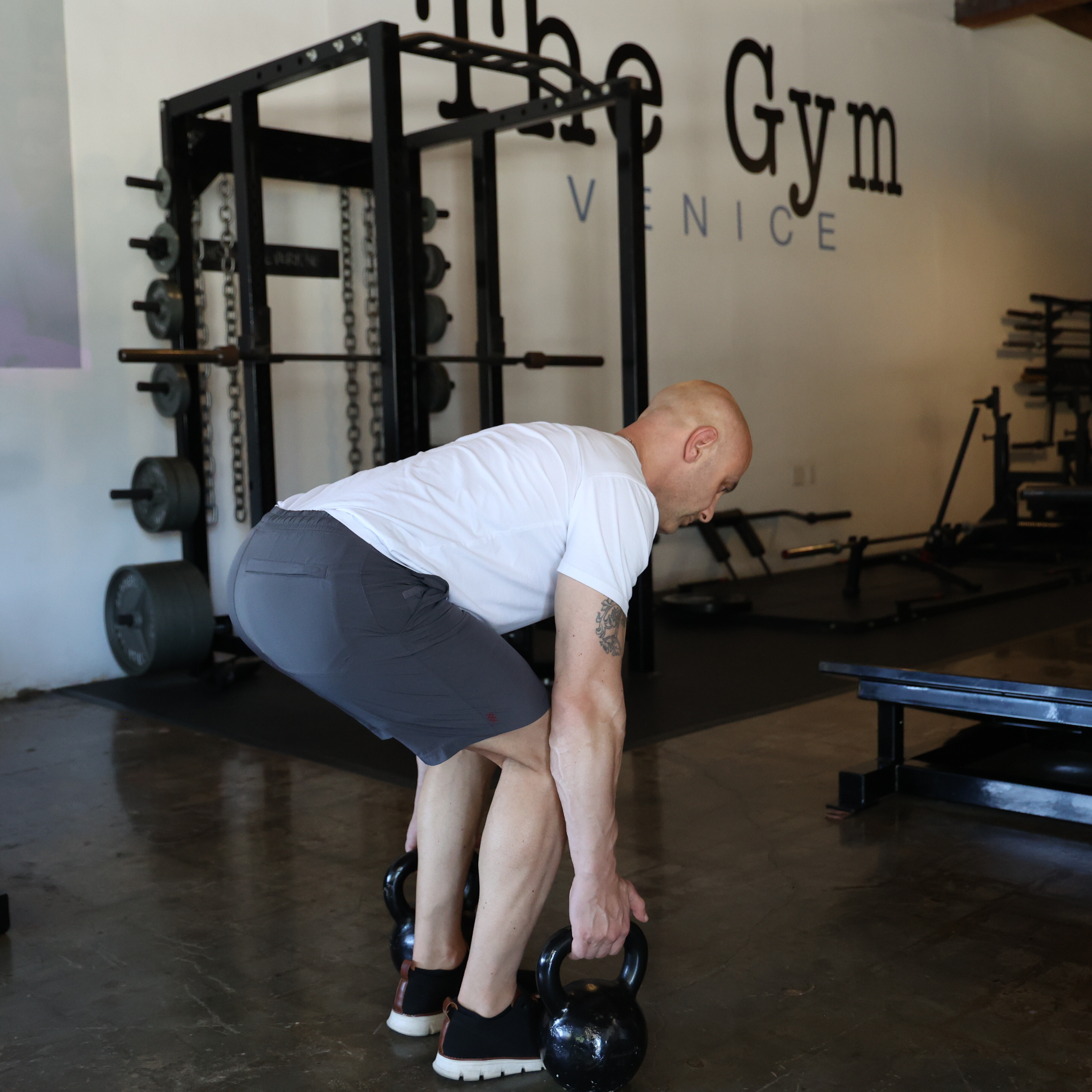 Man demonstrates suitcase deadlift exercise in gym with kettlebells