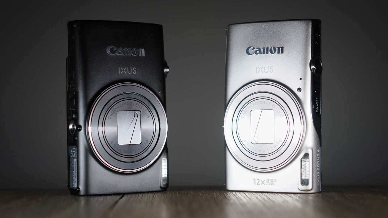 Canon Ixus 285 HS A in black and silver, side-by-side, on a wooden surface against a dark background