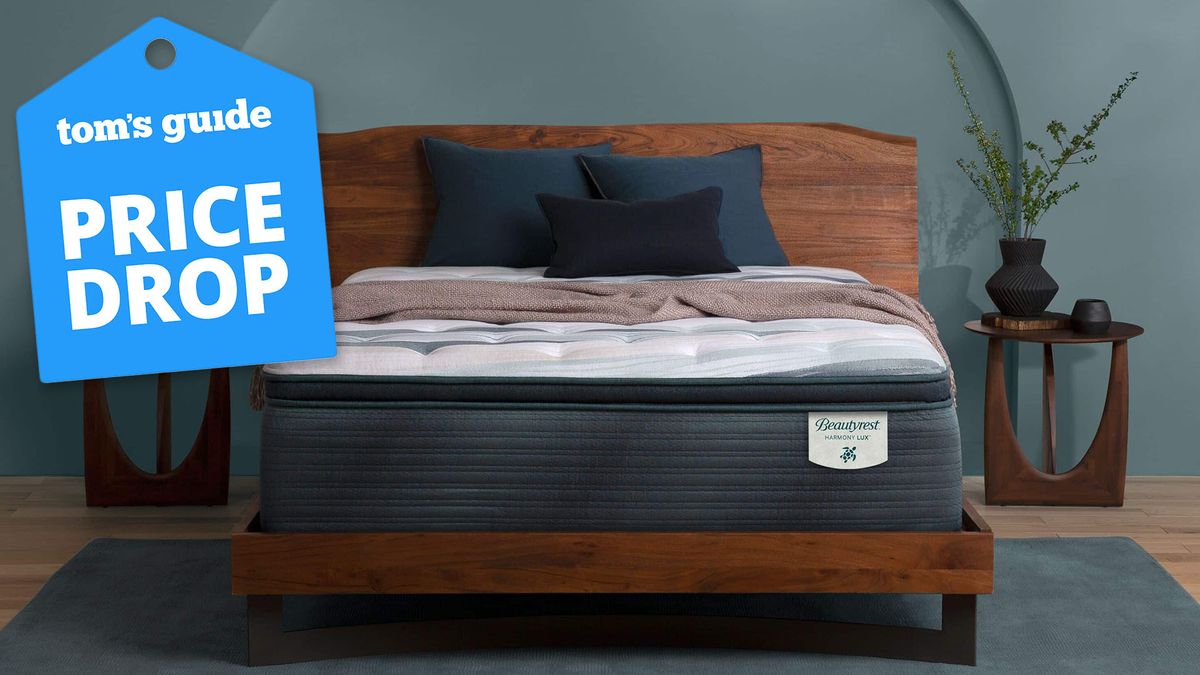 The Beautyrest Harmony Lux mattress on a bedframe in a bedroom, with a Tom&#039;s Guide price drop deals graphic (left)