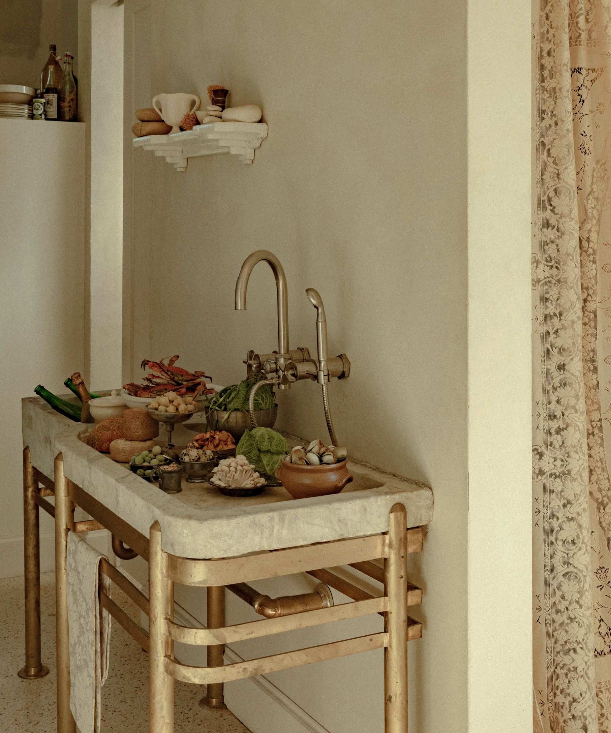 a vintage stone sink sitting on a brass stand in a larder filled with prepared food ready for hosting