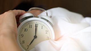How to fix your sleep schedule: A person holds an alarm clock in bed
