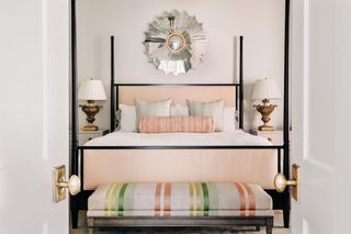 four-poster bed with no drapes with coral cushions and striped ottoman and antique brass bedside lamps