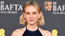 Carey Mulligan is pictured with a wavy bob, with the front strands tucked behind her ears, and wearing silver earrings and a navy Prada dress at the 2026 EE BAFTA Film Awards at The Royal Festival Hall on February 22, 2026 in London, England.