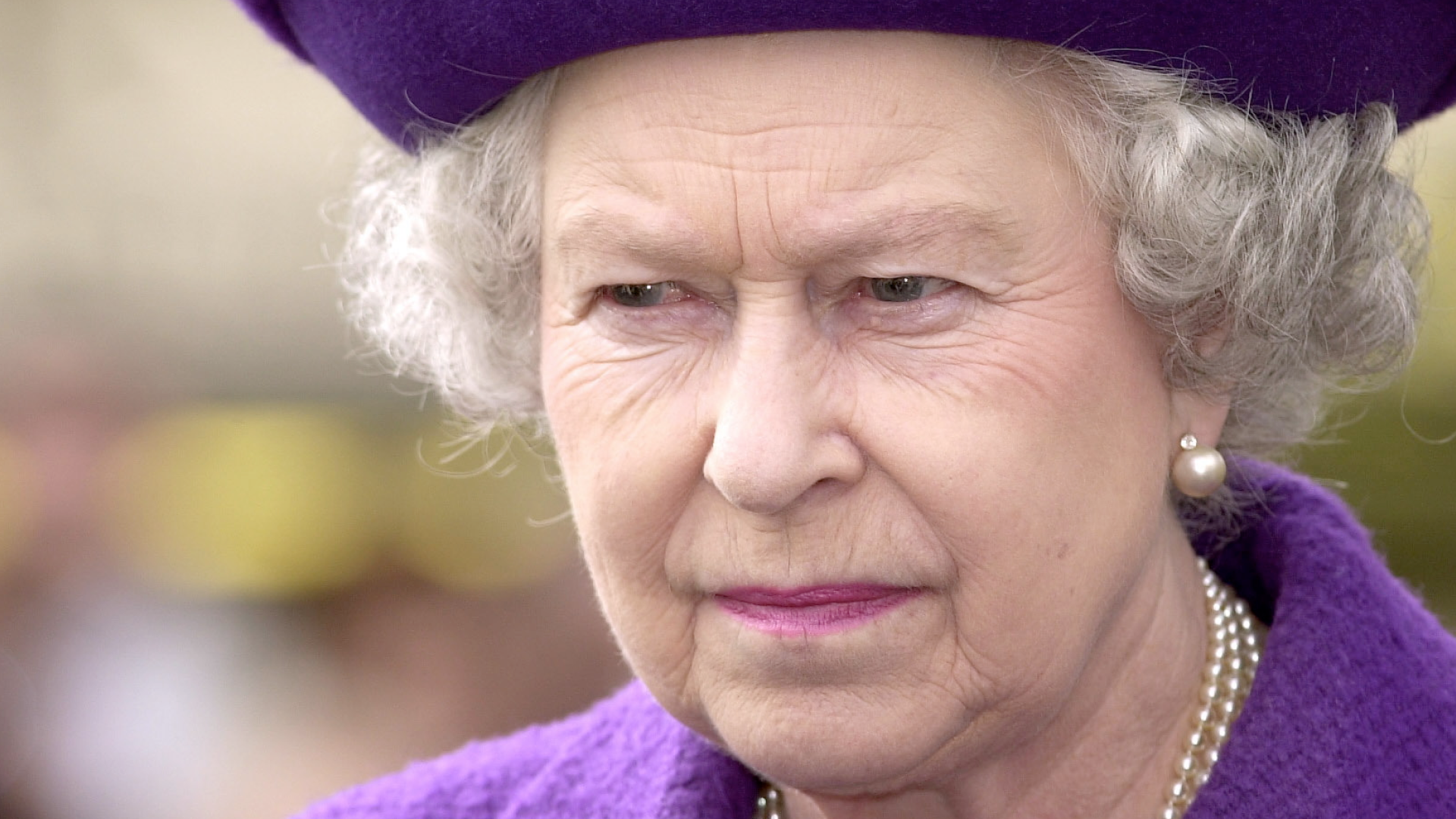 Queen Elizabeth wearing a purple hat and coat scowling