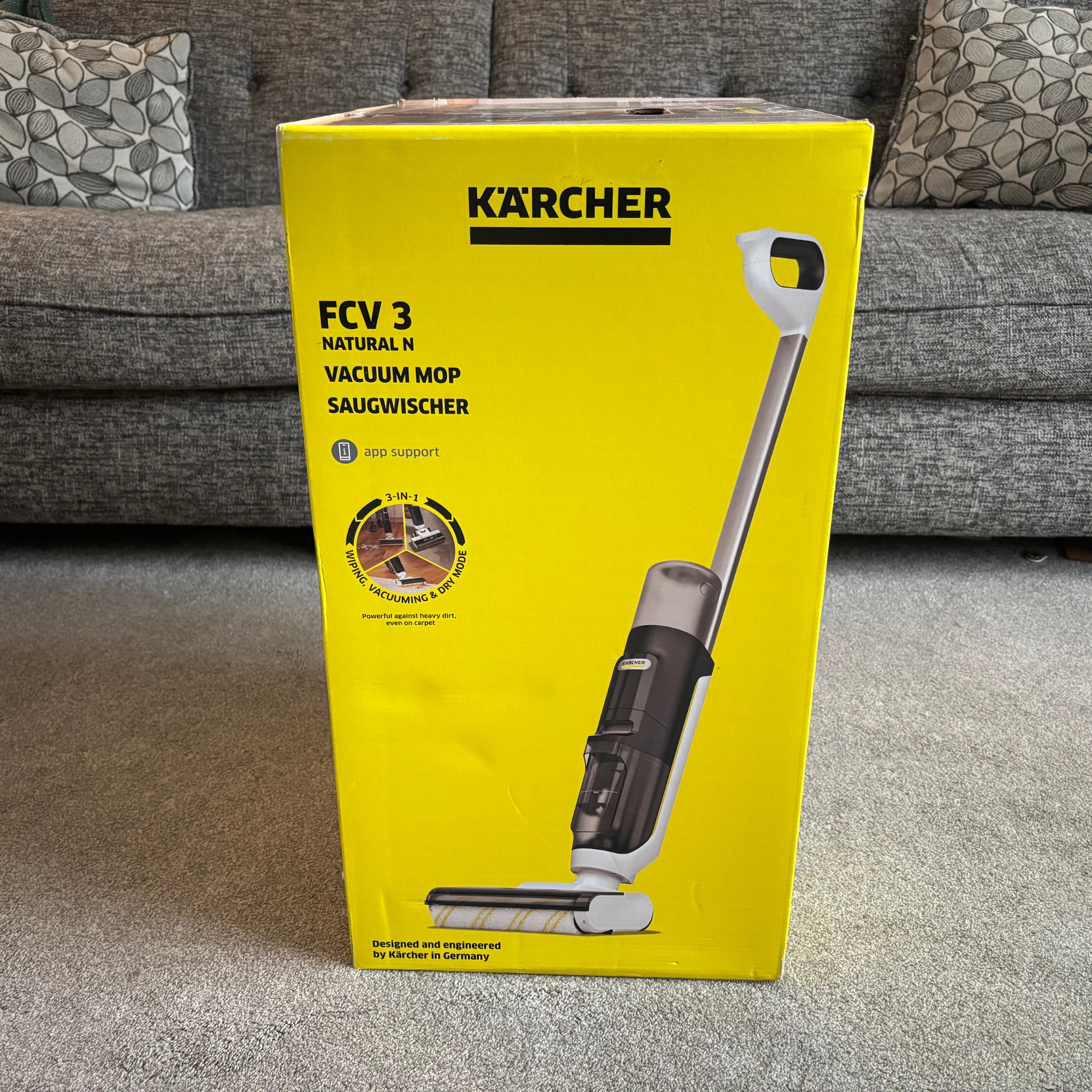 Kärcher Floor Cleaner Vacuum FCV 3 boxed in yellow branded packaging and positioned on carpet in front of sofa