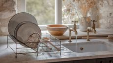 A metal plate drying rack next to sink set into a stone kitchen counter top.