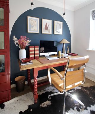 blue arch painted behind desk with red legs and brown leather chair