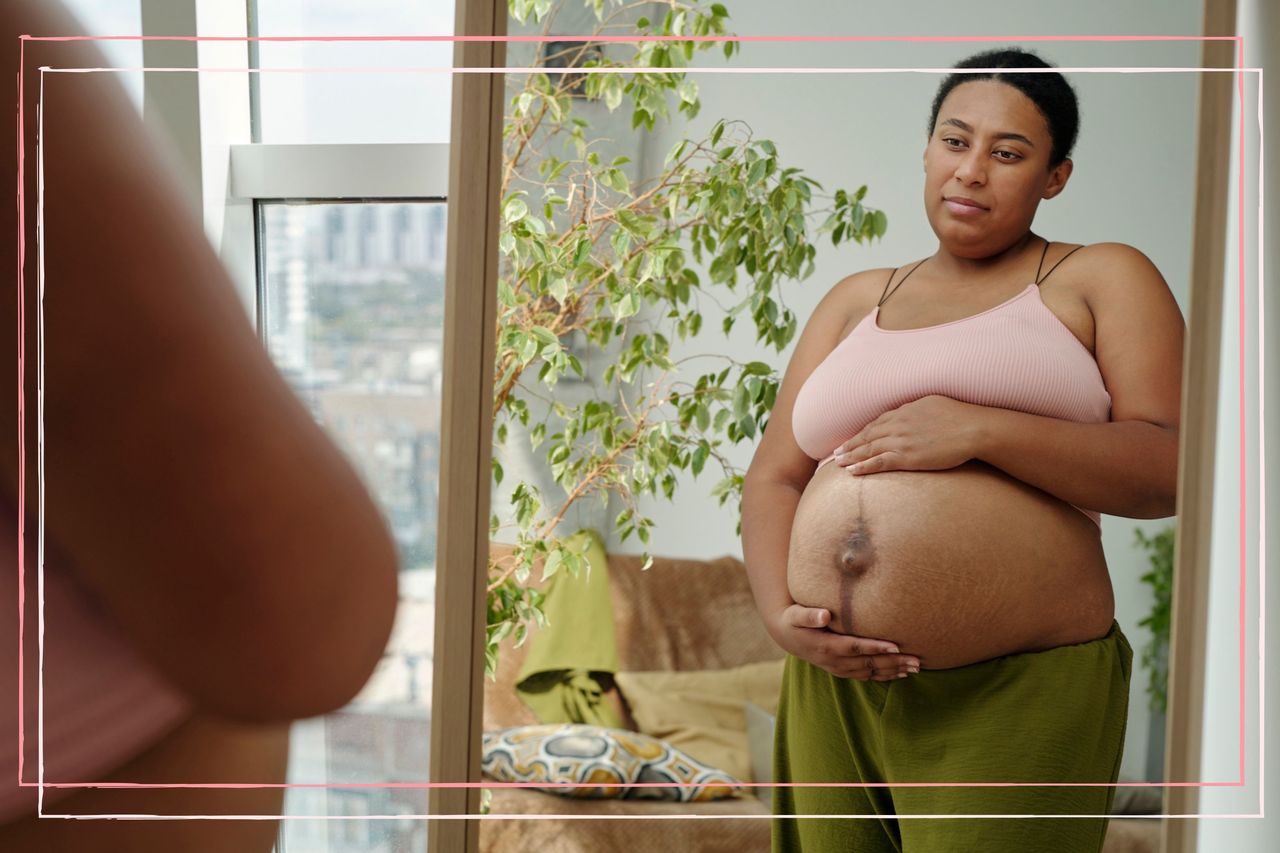 A pregnant woman wearing a crop top and trousers touched her bump whilst looking in the mirror