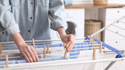 Woman hanging clean laundry on drying rack in bathroom