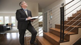 Man standing at foot of staircase with clipboard conducting a homebuyers survey