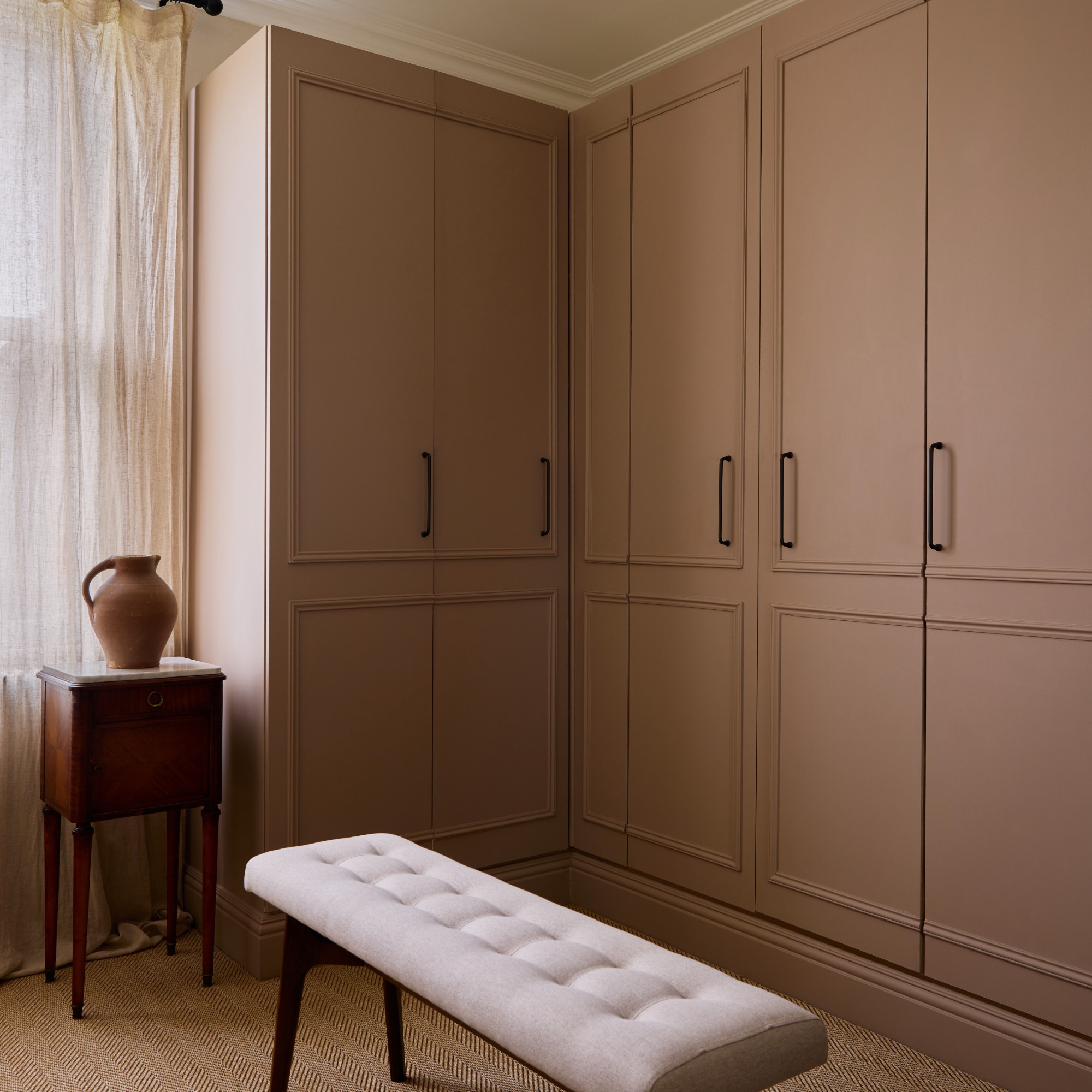 A walk-in closet with built-in wardrobes painted in Farrow &amp;amp; Ball's Dead Salmon and a bench in the middle