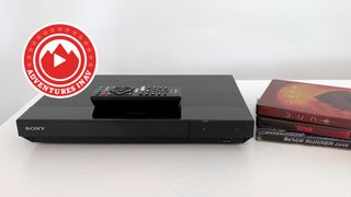 A Sony Blu-ray player sitting on a table with a stack of Blu-ray cases on the right hand side