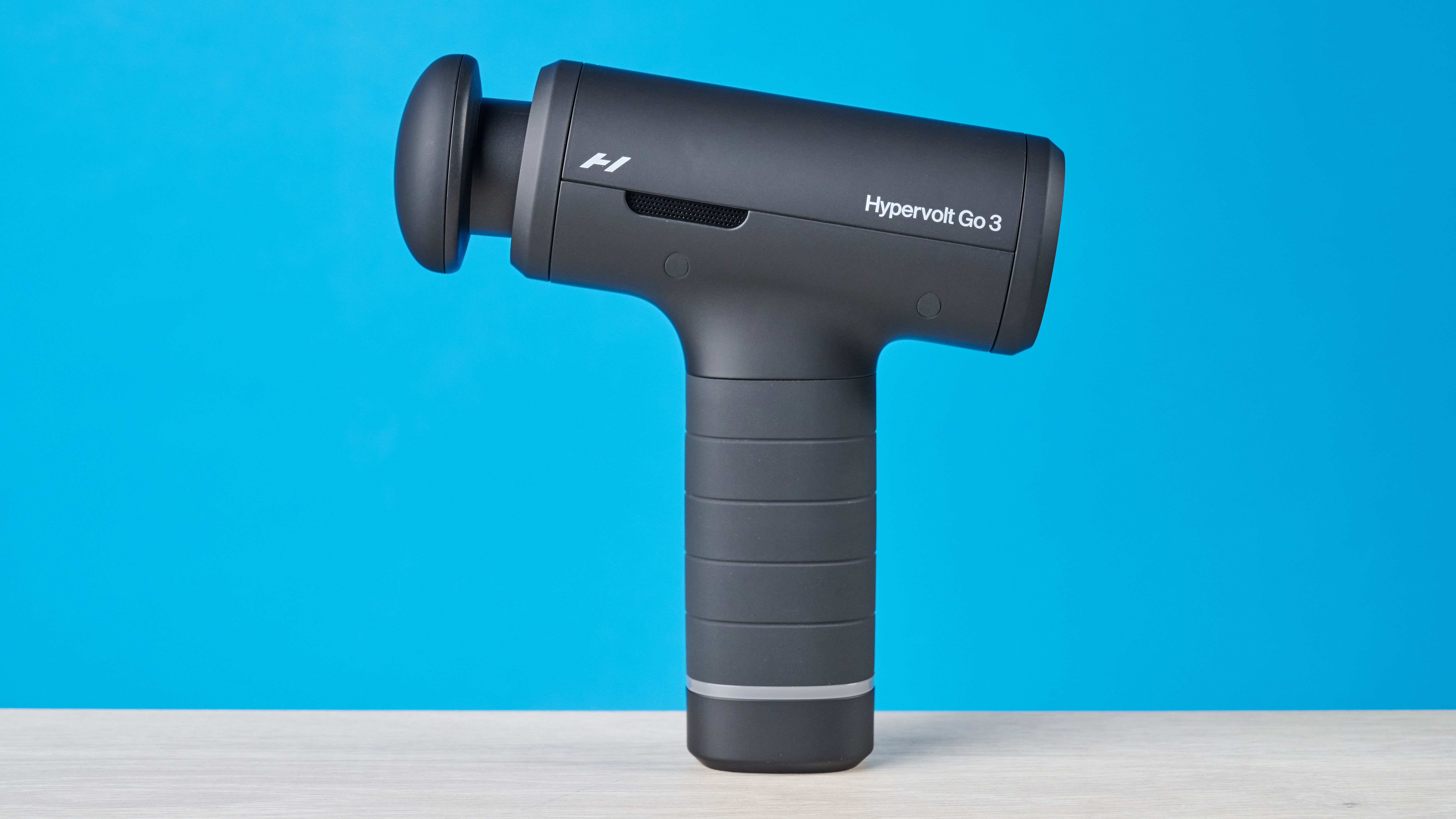 Hyperice Hypervolt Go 3 massage gun photographed in front of a blue background