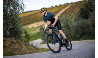 Writer Andy Dilkes is on board the Scott Solace eRide 10 road e-bike out the saddle and climbing a hill with greenary in the background