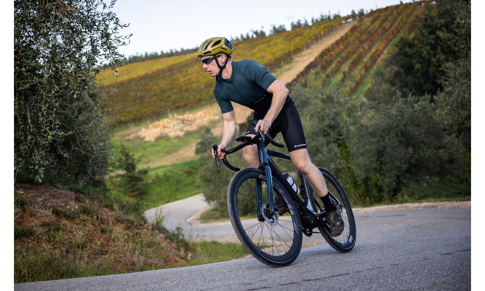 Writer Andy Dilkes is on board the Scott Solace eRide 10 road e-bike out the saddle and climbing a hill with greenary in the background