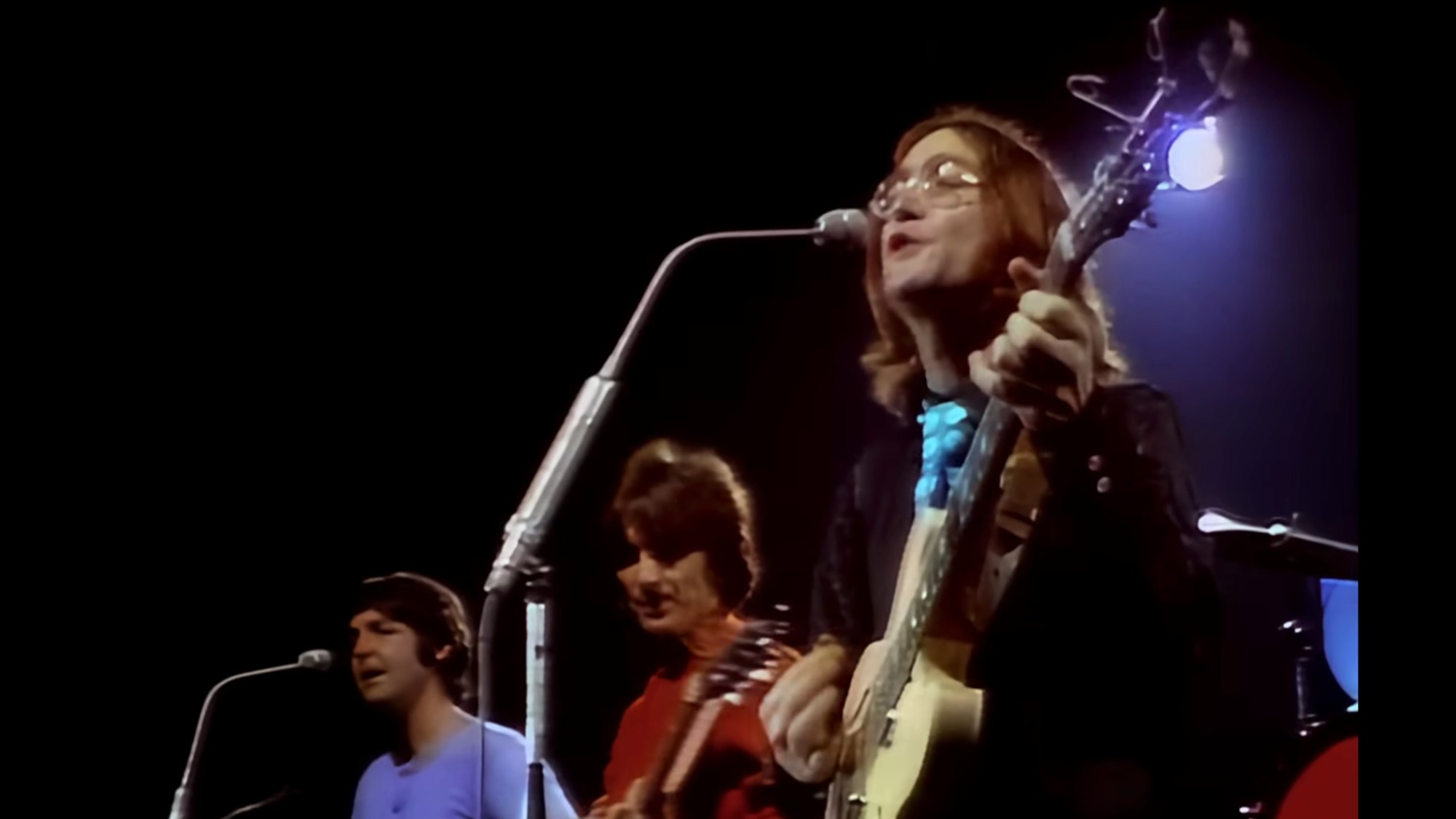 From left to right: Paul McCartney, George Harrison, John Lennon performing on stage.