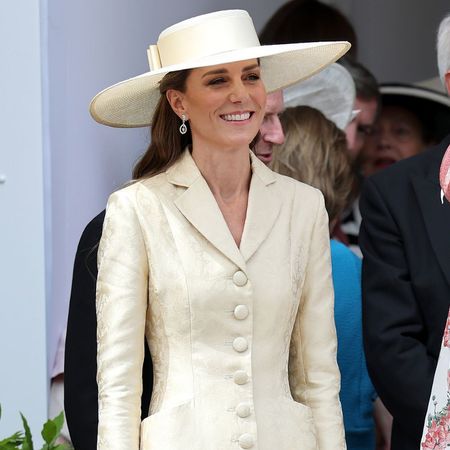Kate Middleton wears a butter yellow coat dress with beige heels and a yellow wide-brim hat.