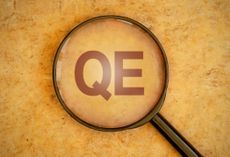 The letters QE, which stand for quantitative easing, under a magnifying glass