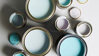Overhead view of open paint tins in blue, teal, grey, and lilac shades on a white surface.