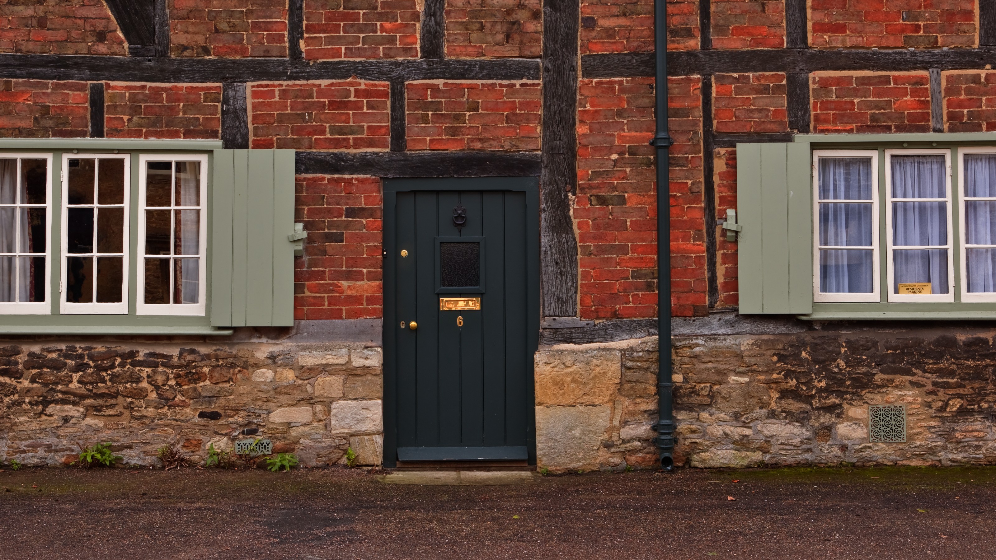 Black front door on old brick cottage, with windows and shutters either side