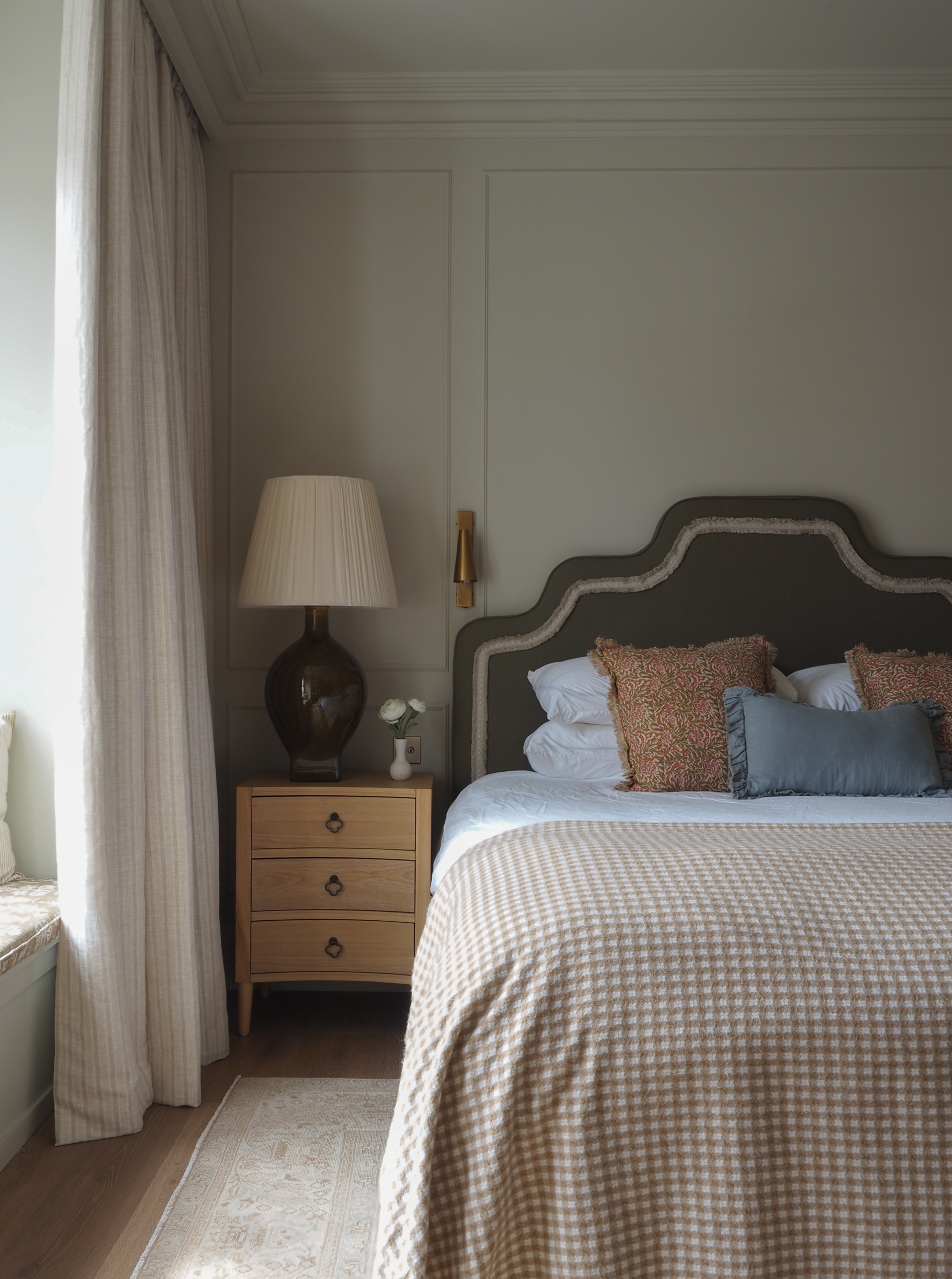 a bedroom with a neutral color scheme, a stepped headboard and a bedside table with a large table lamp