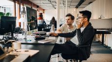 Vibe coding concept image showing two male software developers working on a desktop computer in an open plan office space. 